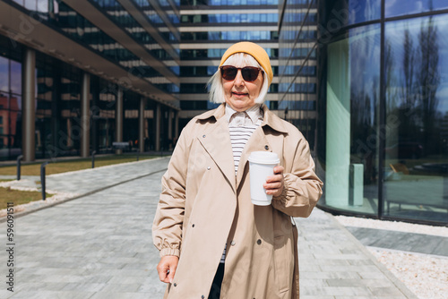 Portrait of Successful Business Woman in yellow hat and sunglasses holding cup of hot drink in hand. Attractive businesswoman drinking a coffee in paper bio white cup. Business on the go concept.