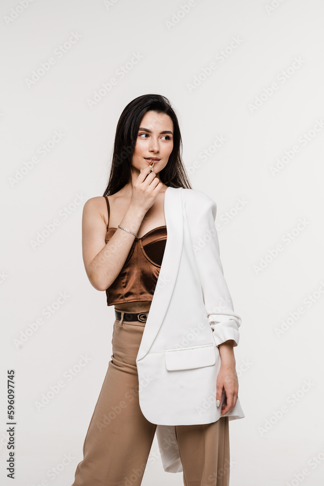 Attractive model is applying matte pastel lipstick on her lips. Girl make-up artist paints her lips with lipstick on white background. Attractive model is applying matte pastel lipstick on her lips. Girl make-up artist paints her lips with lipstick on white background.