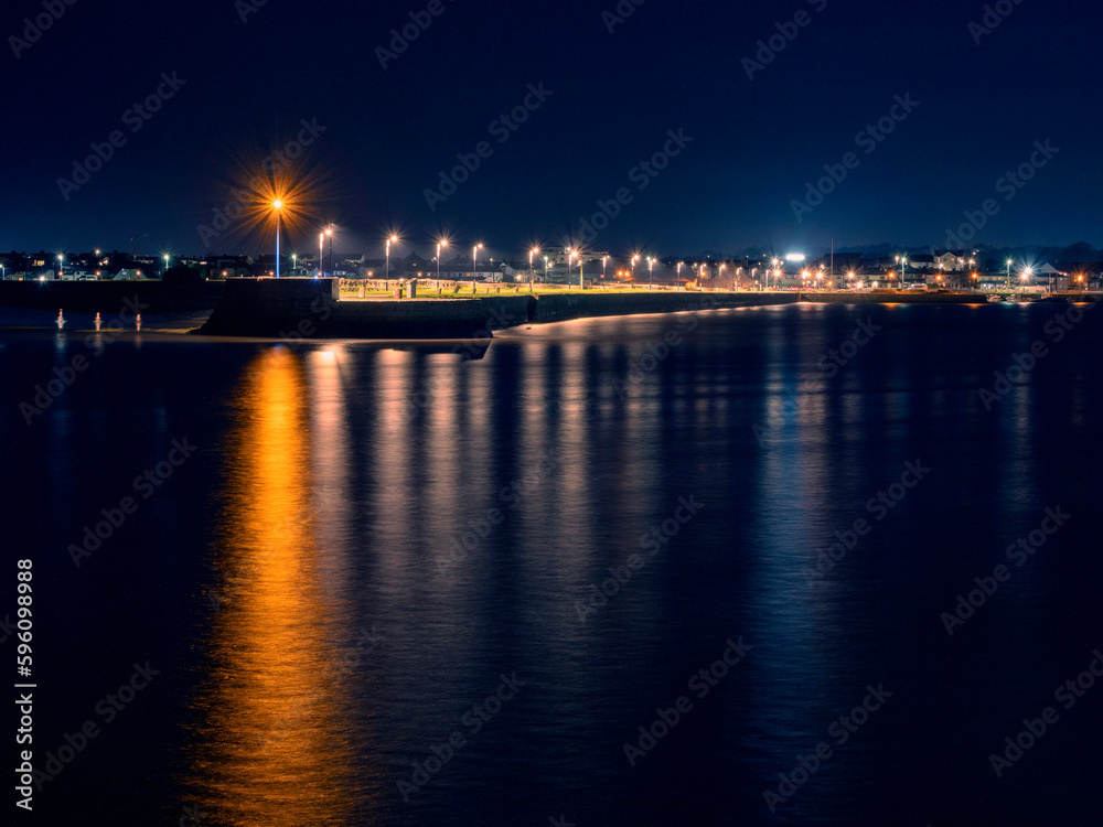 Light on a pier reflecting in water. Galway city, Ireland. Night shot. Town illumination.