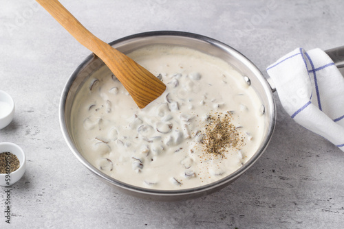 Frying pan with fried mushrooms with onions in bechamel sauce on a gray textured background. Cooking delicious homemade food