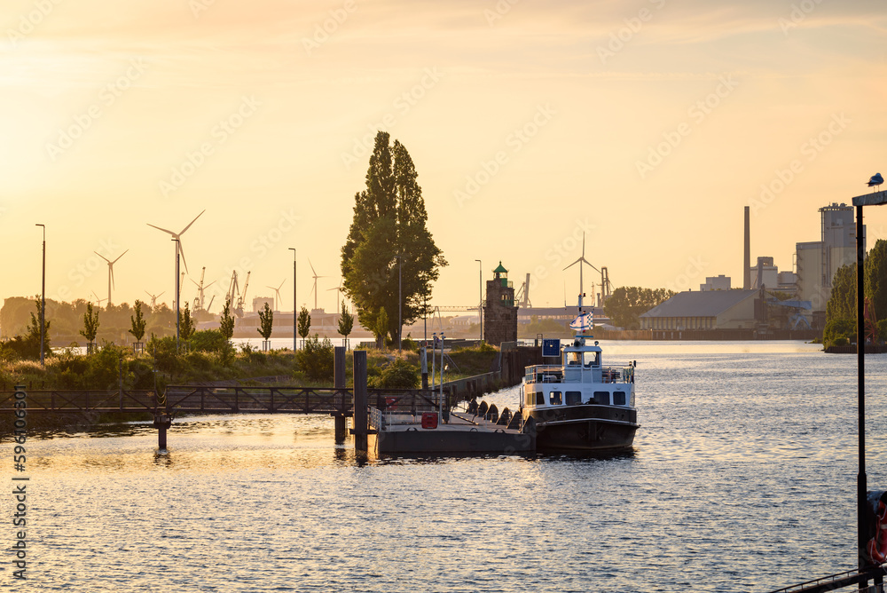 Naklejka premium River harbour at sunset in summer. A lighthouse, industrial plants and wind turbines are visible in background.