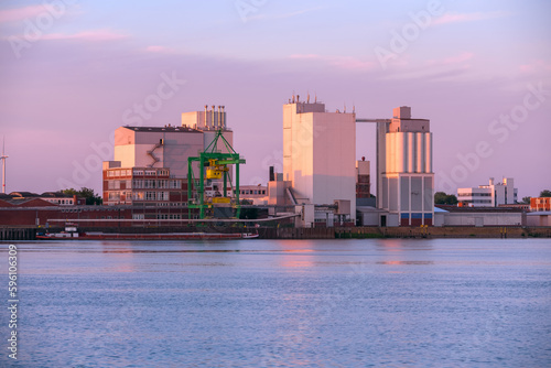 Commercial dock with a gantry crane, silos and warehouses at a river harbour at sunset in summer