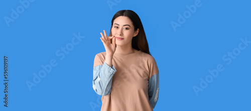 Young Asian woman zipping her mouth on blue background