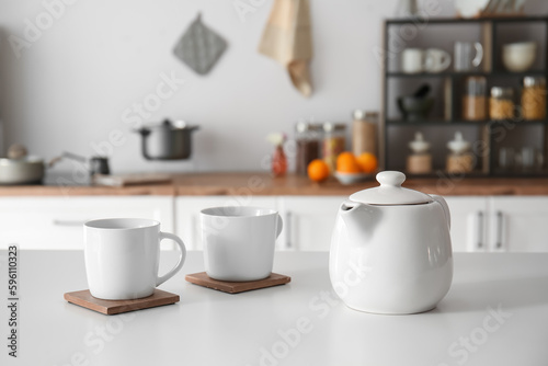 Teapot with cups on table in modern kitchen