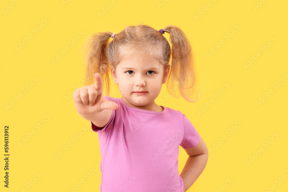 Funny little girl showing loser gesture on yellow background Funny little girl showing loser gesture on yellow background