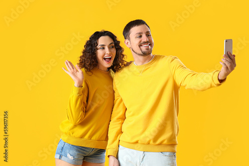 Young couple with mobile phone taking selfie on yellow background