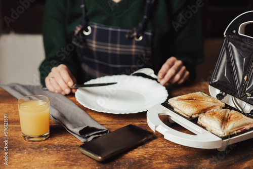 Sandwich and juice. Snack and breakfast preparation. Sandwich maker and unrecognizable woman on wooden background.