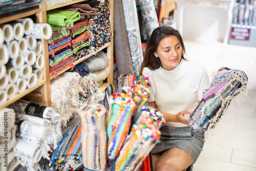Portrait of young adult woman choosing rug at store of household goods