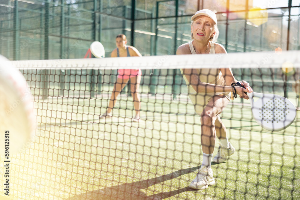 Active aged woman practicing Padel Tennis with other players in the tennis court outdoors