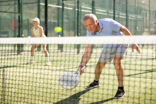 Dynamic old man playing Padel Tennis with partners in the open air tennis court