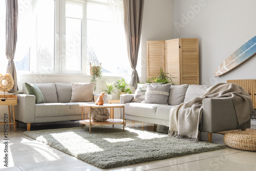 Interior of light living room with surfboard, houseplants and sofas photo