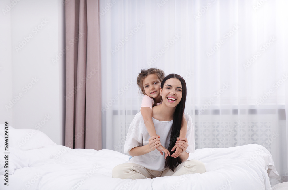 Happy woman and her daughter spending time together on bed at home, space for text. Mother's day celebration Happy woman and her daughter spending time together on bed at home, space for text. Mother's day celebration