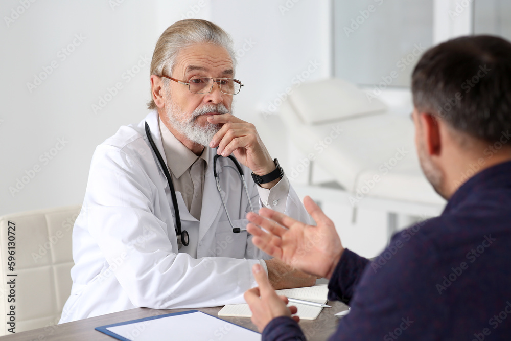 Senior doctor consulting patient at wooden table in clinic Senior doctor consulting patient at wooden table in clinic