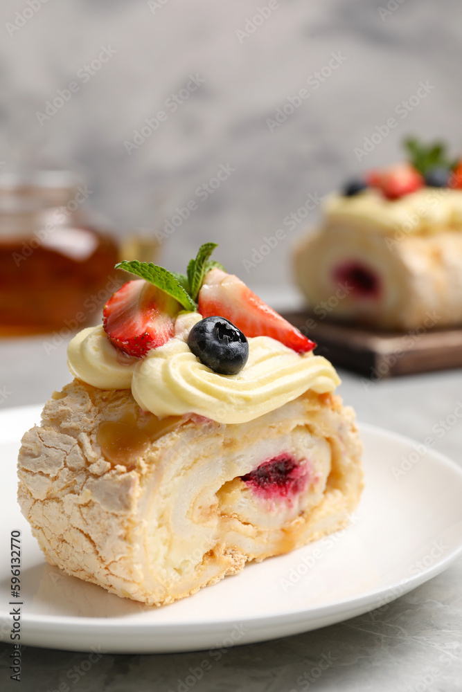 Piece of tasty meringue roll with jam, cream, strawberry, blueberry and mint on light grey table, closeup