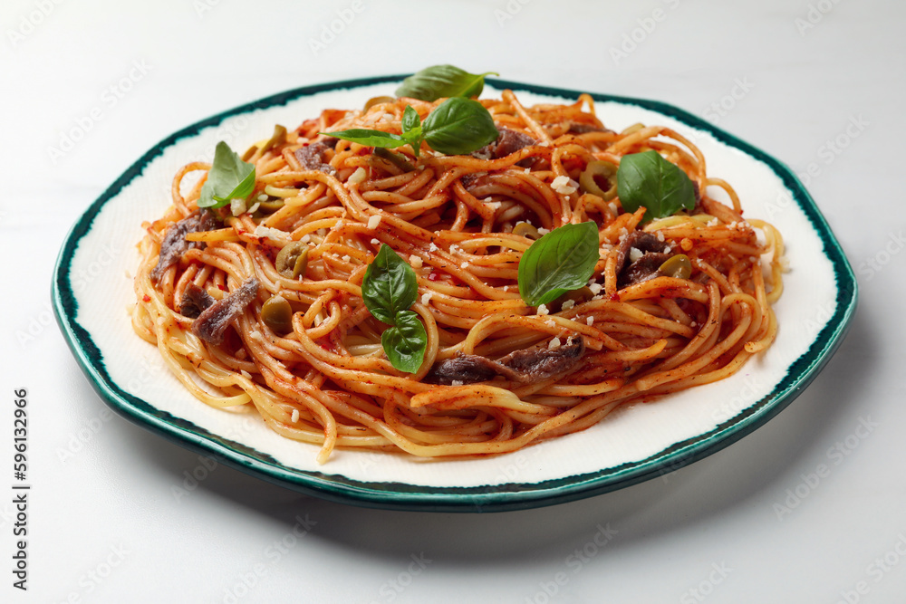 Delicious pasta with anchovies, tomato sauce and basil on white table Delicious pasta with anchovies, tomato sauce and basil on white table