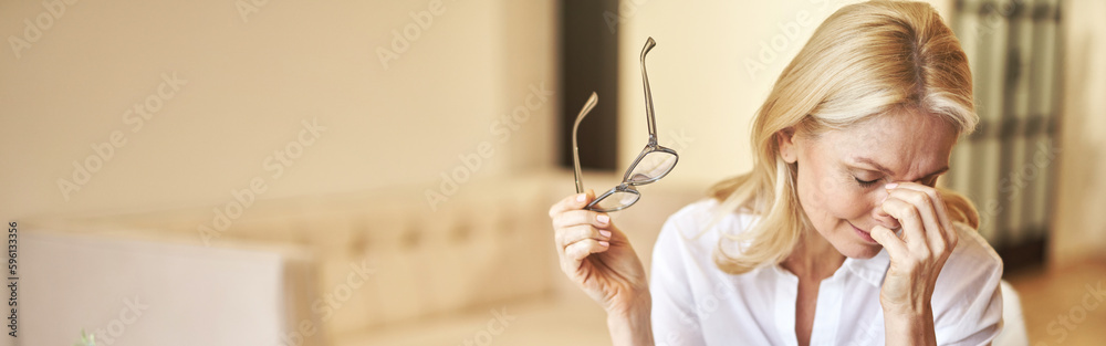 Tired mature businesswoman took off her glasses, massaging nose bridge, suffering from dry eyes syndrome Tired mature businesswoman took off her glasses, massaging nose bridge, suffering from dry eyes syndrome