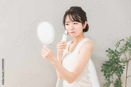 鏡を見ながらウォーターピーラーを使う肌荒れに悩む・困るアジア人女性  © buritora