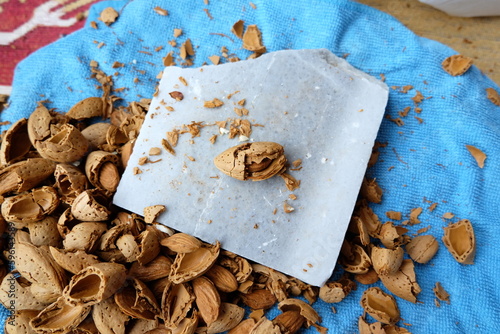 Shelling almonds on a colorful blue background outdoors, selective focus. Cracking and picking up almond. Raw Almond shell background with nut shell cracker hammer. It is not grain, its texture of it.