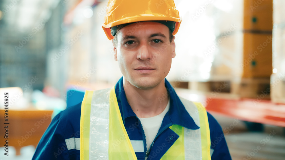 Handsome man and happy professional worker wearing safety vest and hard hat, Smiling to camera. Big warehouse with shelves full of stock Handsome man and happy professional worker wearing safety vest and hard hat, Smiling to camera. Big warehouse with shelves full of stock