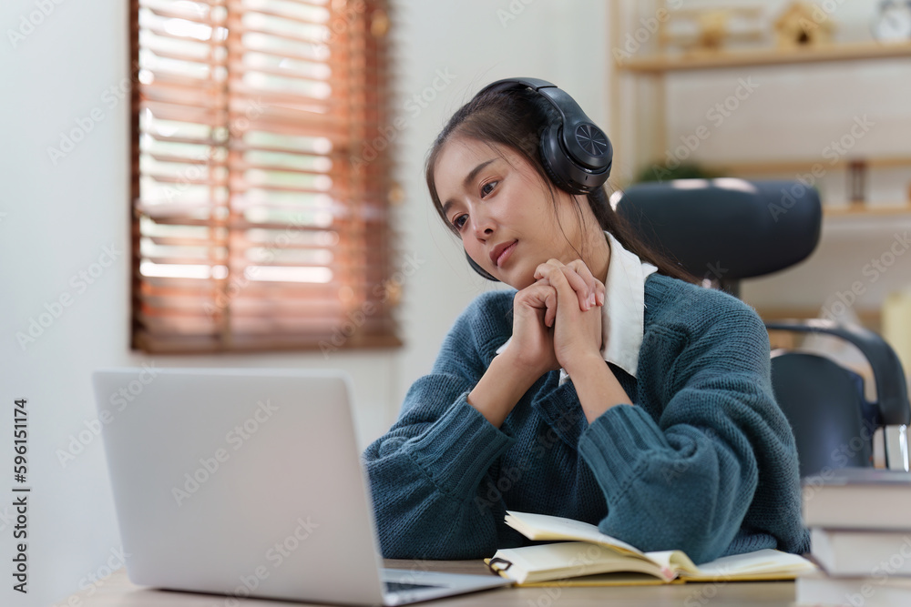 Online education, e-learning. Asian woman relaxing after studying using a laptop, listening to online lecture, taking notes, online study at home Online education, e-learning. Asian woman relaxing after studying using a laptop, listening to online lecture, taking notes, online study at home