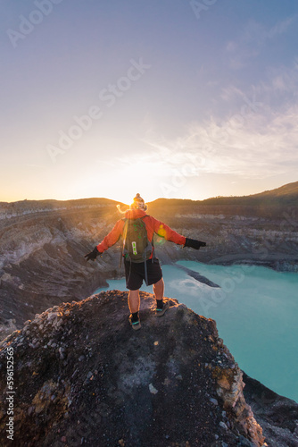vertical shot of man contemplating the Poas Volcano Crater Lagoon at sunrise surrounded by volcanic rocks in the Poas Volcano National Park in the Alajuela province of Costa Rica