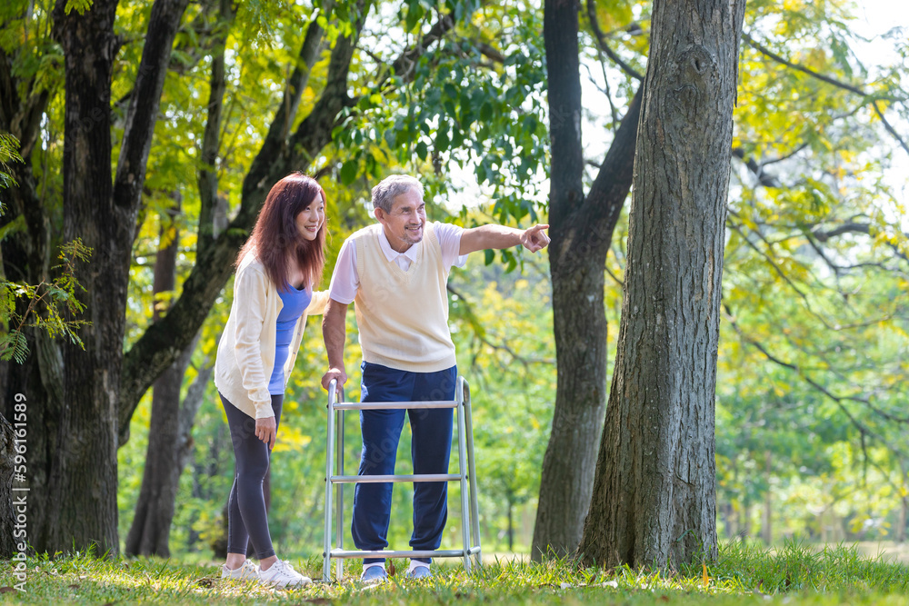 Asian senior man with walker and his daughter walking together in the park looking for beautiful nature and wildlife during summer for light exercise and physical therapy concept