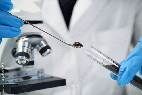 Scientist takes black soil from test tube with little spoon