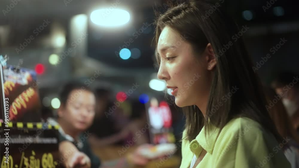 Solo traveler asian women enjoy buying and eating traditional street food night market. Beautiful Tourists woman feeling happy buying street food in the evening. Street food concept.