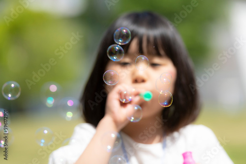 新緑の初夏の公園でシャボン玉をして遊ぶ女の子