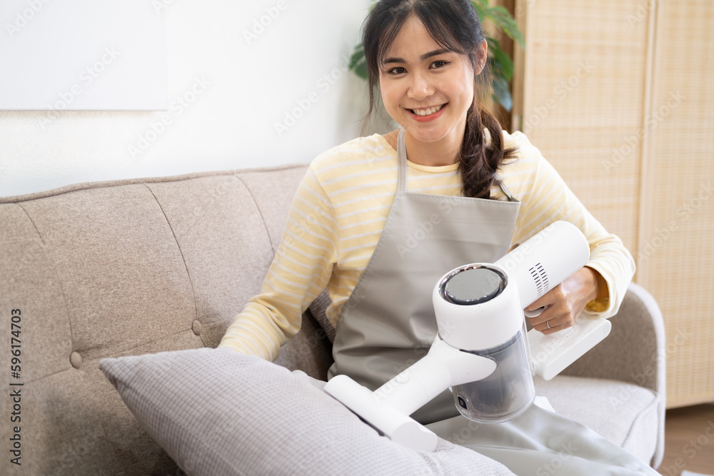 Young Smiling Woman in Apron Cleaning House. Happy Beautiful Girl Cleaning sofa in living room.Young woman cleaning her Apartment. Young Smiling Woman in Apron Cleaning House. Happy Beautiful Girl Cleaning sofa in living room.Young woman cleaning her Apartment.