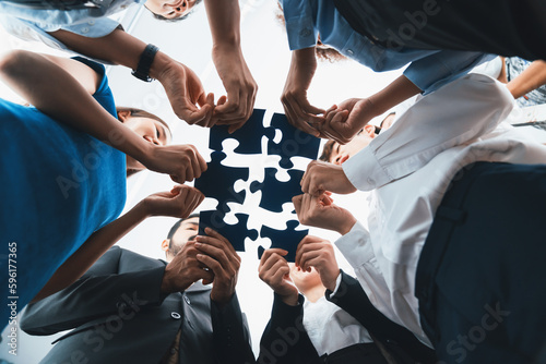 Below view of diverse corporate officer workers collaborate in office connecting puzzle pieces as partnership and teamwork concept. Unity and synergy in business idea by merging jigsaw puzzle. Concord photo