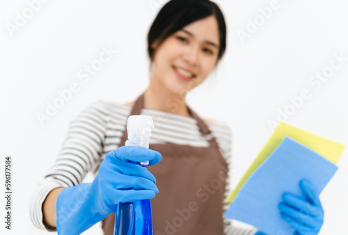 Happy young woman wearing blue rubber gloves for hands protection , holding sponge and spray bottle , smiling at camera while cleaning house isolated over white background