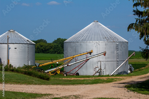 Landscape view of a round silver corrugated steel agricultural crop storage bin with farm machinery in the foreground © Cynthia