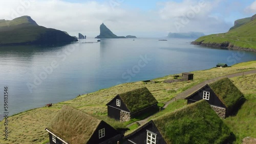 4k drone forward video (Ultra High Definition) of Bour village with typical turf-top houses and Tindholmur cliffs on background. Aerial morning view of Vagar island, Faroe, Denmark, Europe.