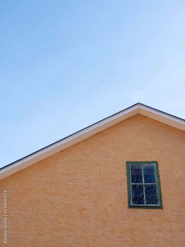 The facade and roof of an old yellow house against a white sky The facade and roof of an old yellow house against a white sky