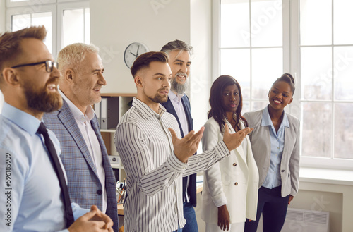 Group of business people listening to their colleague or their leadership at working place. Company employees on meeting standing in office. Cowokers discussing work project or greeting new employee.