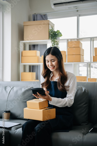 .Young business owner woman prepare parcel box and standing check online orders for deliver to customer on tablet, laptop Shopping Online concept. © laddawan