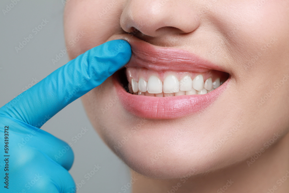Doctor examining woman's gums on grey background, closeup Doctor examining woman's gums on grey background, closeup