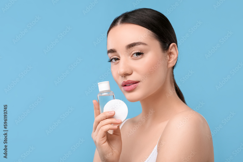Beautiful woman with makeup remover and cotton pad on light blue background, space for text Beautiful woman with makeup remover and cotton pad on light blue background, space for text