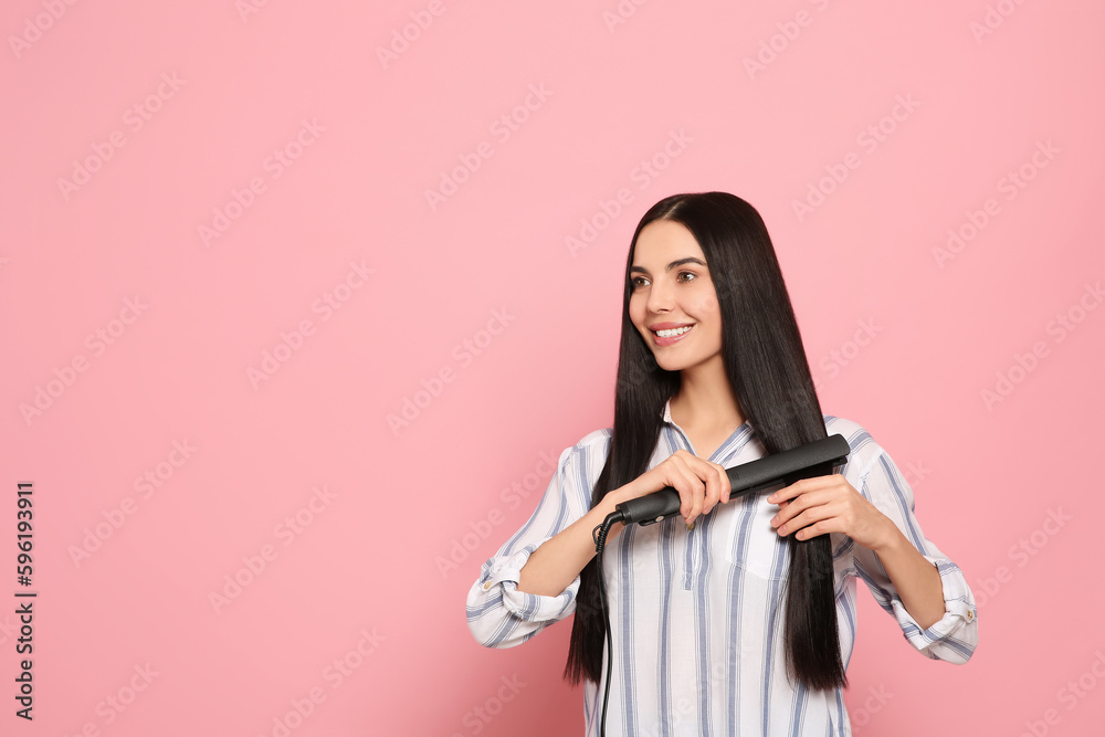 Beautiful happy woman using hair iron on pink background. Space for text Beautiful happy woman using hair iron on pink background. Space for text