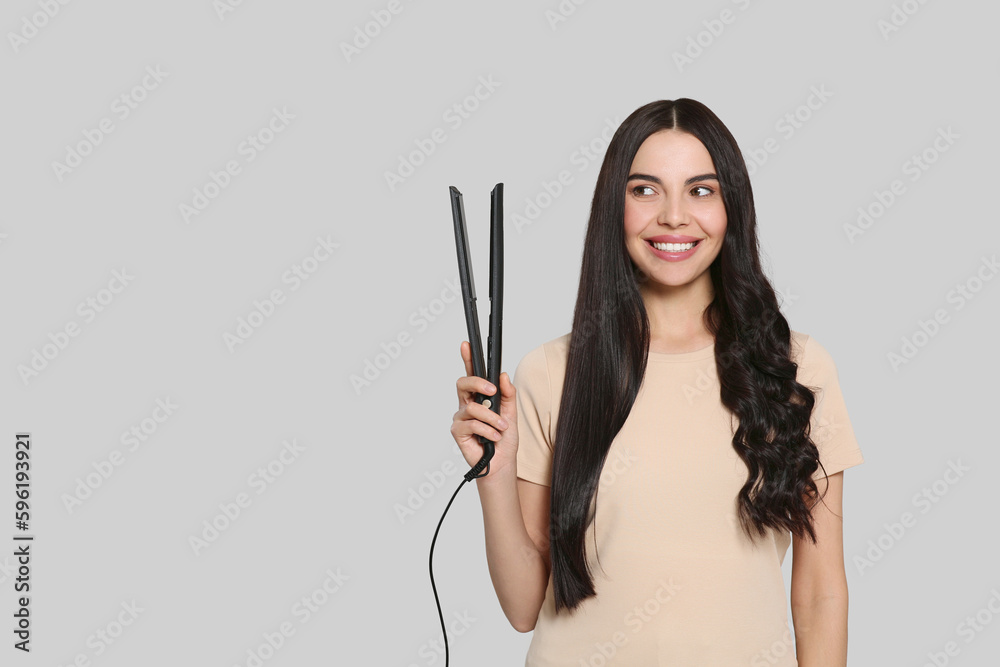Beautiful happy woman with hair iron on light grey background. Space for text Beautiful happy woman with hair iron on light grey background. Space for text