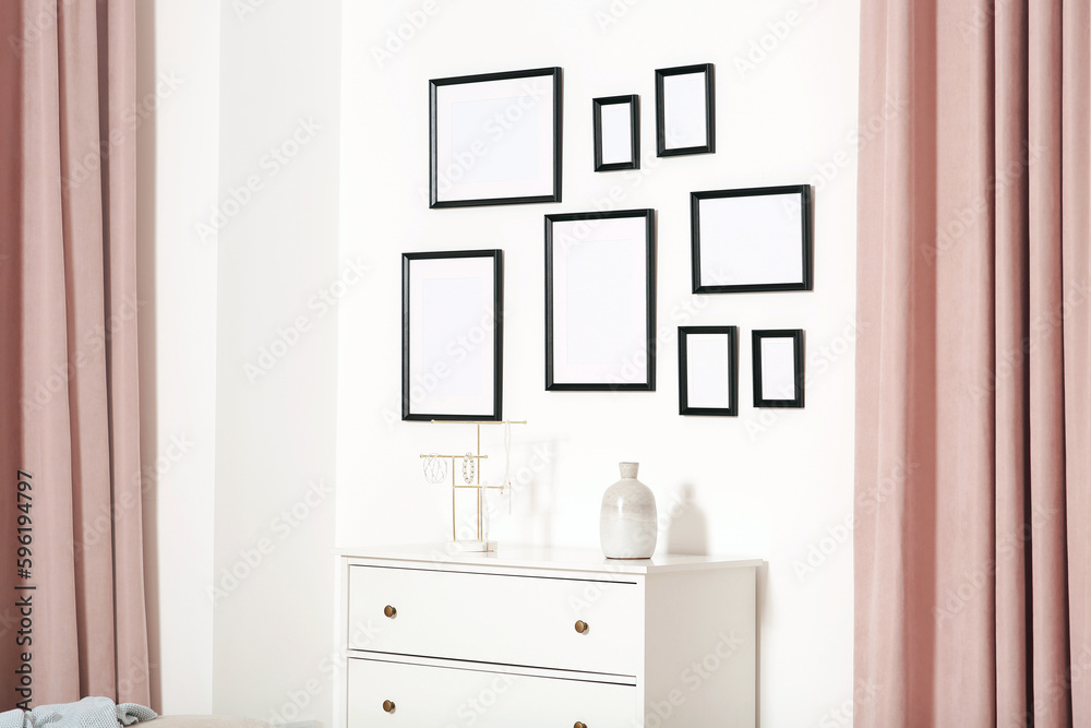 Empty frames hanging on white wall and chest of drawers indoors Empty frames hanging on white wall and chest of drawers indoors