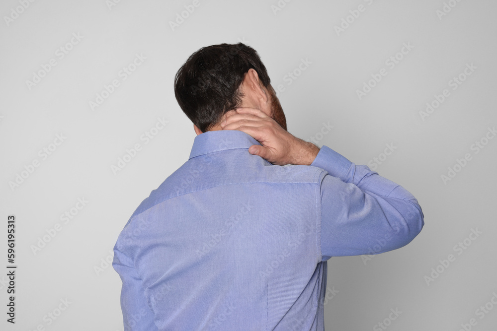 Man suffering from pain in his neck on light background, back view. Arthritis symptoms Man suffering from pain in his neck on light background, back view. Arthritis symptoms