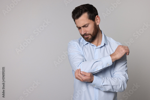 Man suffering from pain in his elbow on light background, space for text. Arthritis symptoms