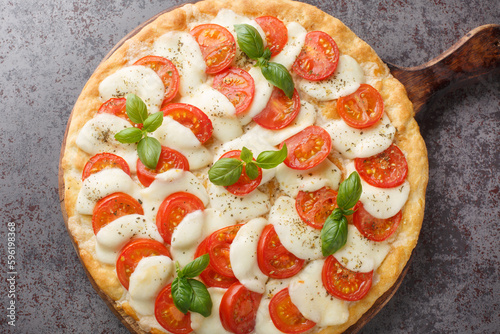 Delicious hot caprese pizza with mozzarella, tomatoes and basil leaves close-up on a wooden board on the table. horizontal top view from above