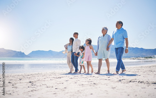 Family, holding hands and walking at beach for mockup space by sea, sand or bond with love on summer vacation. Men, women and children for support, holiday and ocean mock up with waves in sunshine