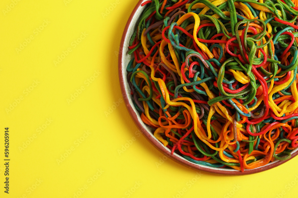 Plate of spaghetti painted with different food colorings on yellow background, top view. Space for text