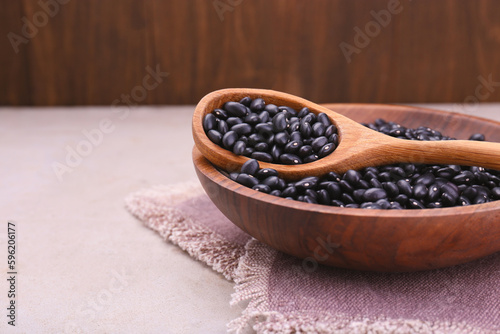 Bowl and spoon of raw black beans on light grey table, closeup. Space for text
