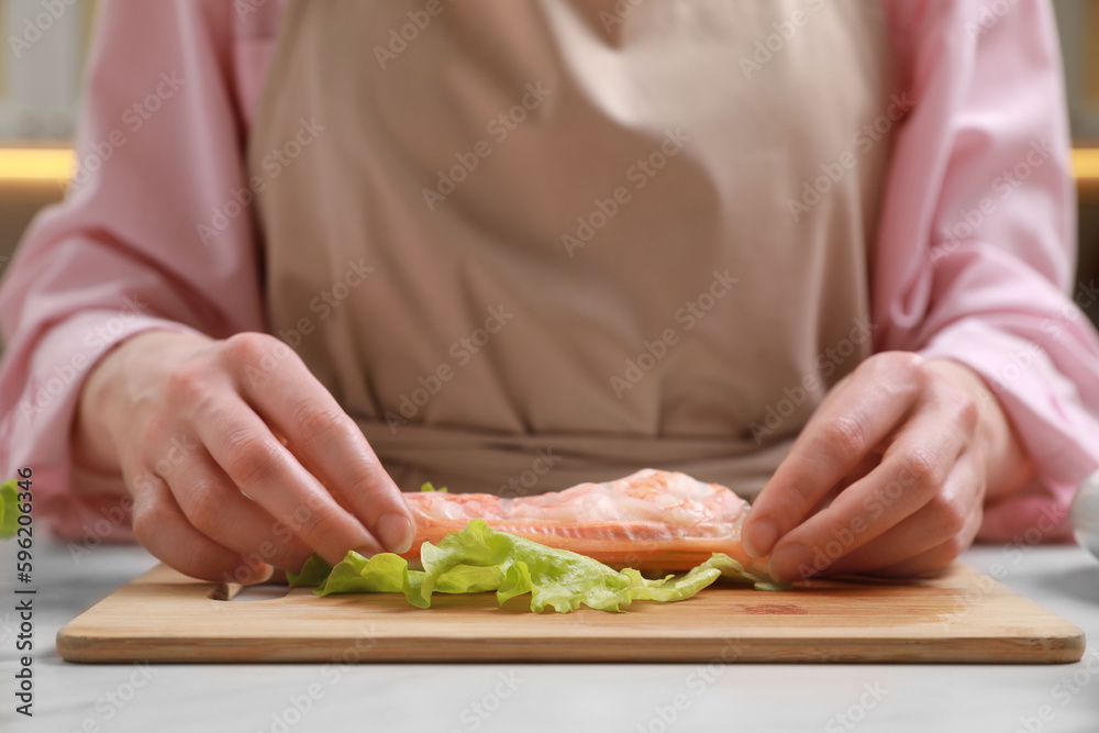 Woman making delicious spring roll at white table, closeup