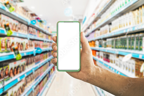 Smartphone and shopping. Hand with a blank smartphone screen on the background of the supermarket counters. App, shopping, grocery concept.
